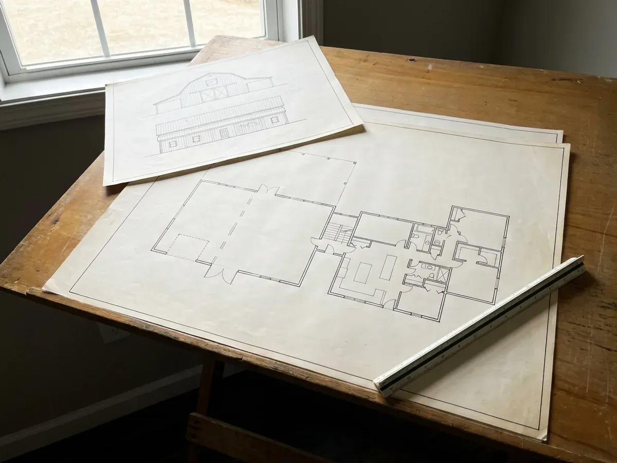 Barndominium floor plan and elevation drawings laid out on a drafting table with a scale rule.